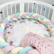 Pastel braided crib bumper with pink blanket inside a crib