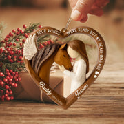 Heart-shaped memorial ornament with a woman holding a horse, surrounded by red berries on a wooden surface.